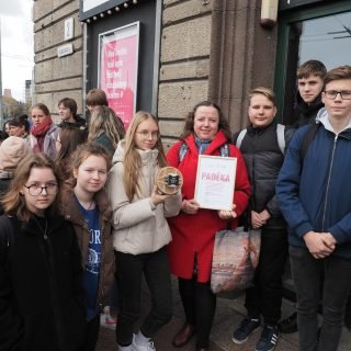 Mokinių grupė su mokytoja pozuoja prie Skallvijos kino teatro su padėka