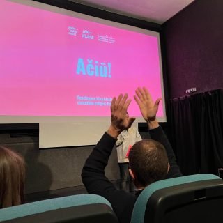 Skalvijos salės ekrane rodoma skaidrė, kurioje pažymėtas projekto rėmėjas (Aktyvių piliečių fondas) bei Nepatoguas kino ir Nepatogaus kino klasės logotipai, didelėmis raidėmis parašytas žodis "Ačiū" ir plojantis žmogus sėdintis priekyje